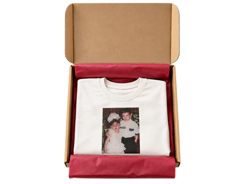 Un t-shirt blanc personnalisé, soigneusement plié dans un carton ouvert avec du papier de soie bordeaux
